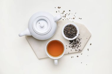 Çaydanlıklı kompozisyon, bir fincan çay ve beyaz arka planda kuru yapraklar.