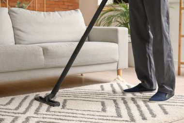 Adam oturma odasında güzel halı temizliyor.