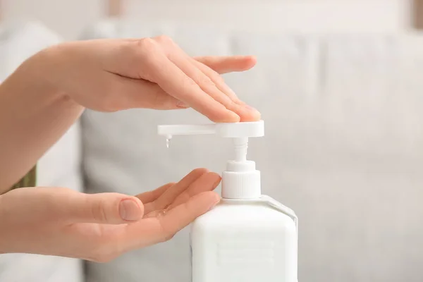 Young woman using sanitizer at home, closeup