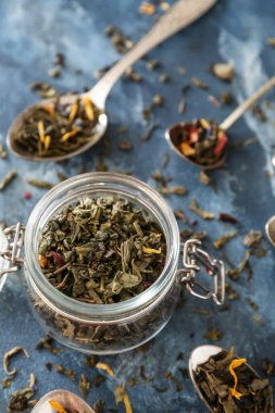 Arkaplanda yeşil çay yapraklı kavanozlar ve kaşıklar