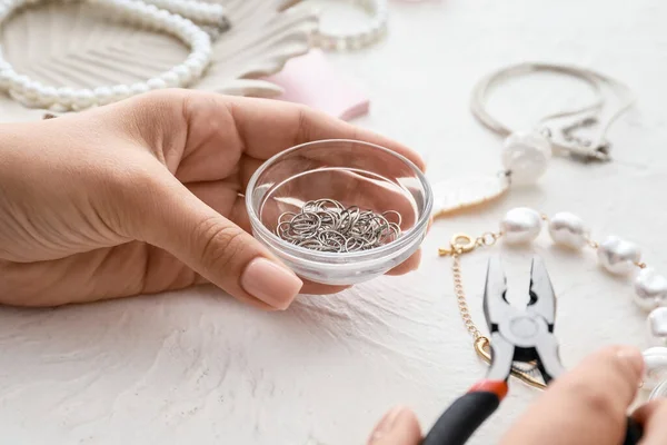 Female designer making jewelry on light background