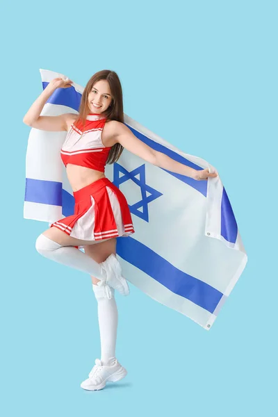 Beautiful young cheerleader with the flag of Israel on color background