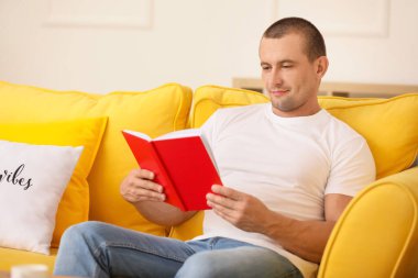 Adam evde kitap okuyor.