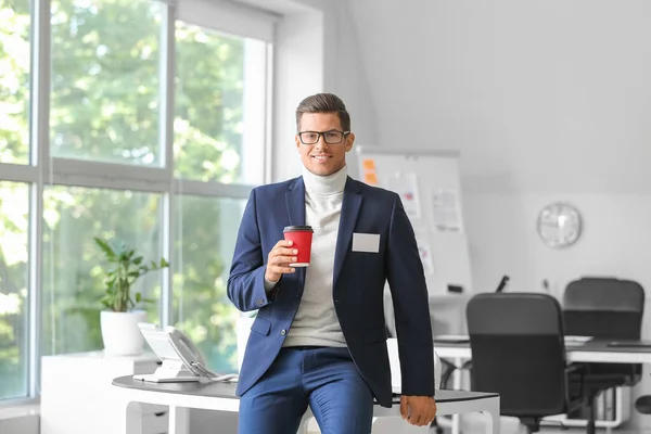 Elegant man in suit with blank badge and takeaway cup in office