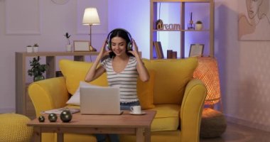 Bilgisayarlı, müzik dinleyen ve akşamları evde kahve içen güzel genç bir kadın.