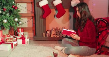 Noel arifesinde şöminenin yanında kitap okuyan bir kadın.