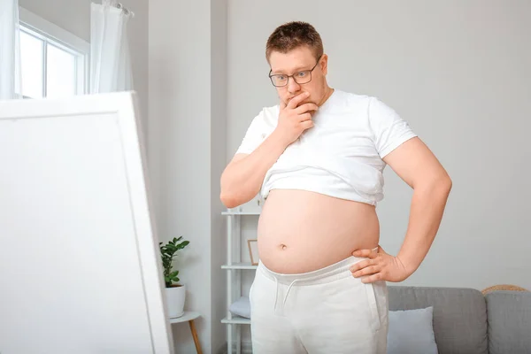 Stressed overweight man near mirror at home. Weight loss concept