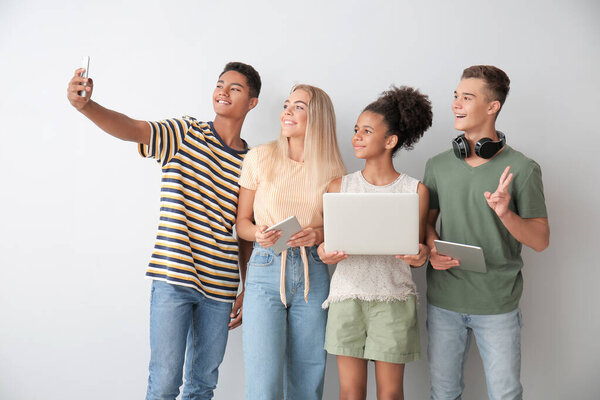 Teenagers with different devices taking selfie on light background
