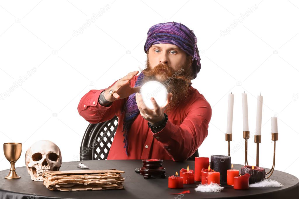 Male fortune teller with crystal ball at table on white background