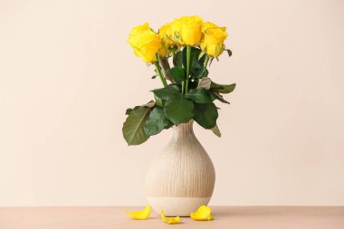 Masada açık arkaplanda güzel sarı güller olan vazo.