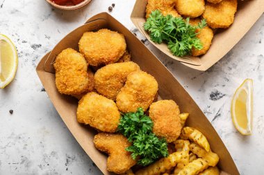 Lezzetli nuggetlar ve kızarmış patatesler arka planda karton kutuda.