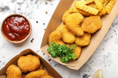 Lezzetli nuggetlar ve kızarmış patatesler arka planda karton kutuda.