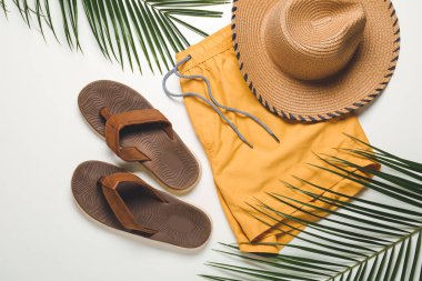 Beyaz arka planda erkek mayosu, şapka ve parmak arası terlikler.