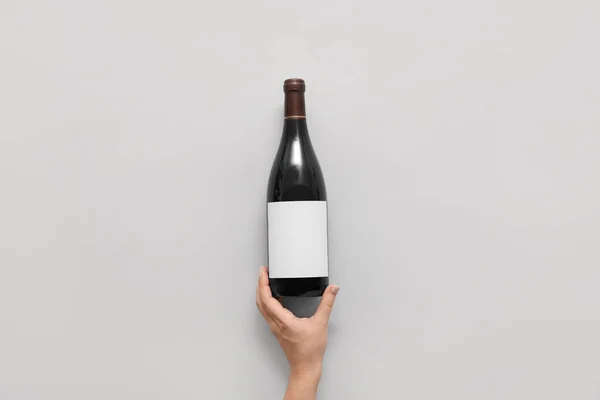 Γυναικείο Χέρι Και Μπουκάλι Κρασί Λευκή Ετικέτα Στο Φως Φόντο — Φωτογραφία Αρχείου