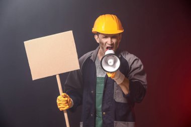 Karanlık arka planda megafon ve afişi olan madenciyi protesto ediyor.