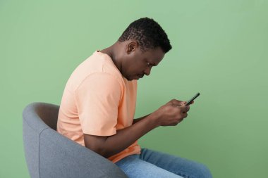 Kambur, cep telefonu olan, renkli duvarın yanında oturan Afro-Amerikan bir adam.