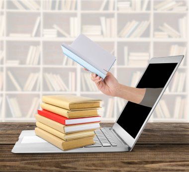 Masada yığınla kitap ve laptop var. Çevrimiçi kitaplık kavramı