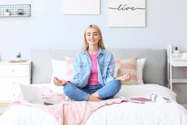 Genç ve güzel bir kadın yatak odasında meditasyon yapıyor.