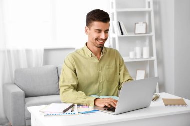 Evde dizüstü bilgisayarı olan genç bir adam.