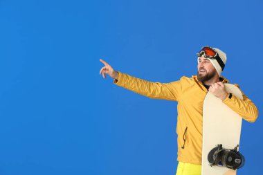 Erkek snowboardcu renk arkaplanındaki bir şeyi işaret ediyor