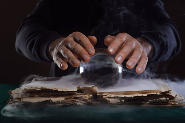 Fortune teller with crystal ball and book at table