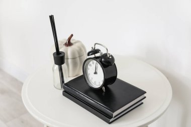 Kitaplı masa, alarm saati ve beyaz duvarın yanındaki dekor.