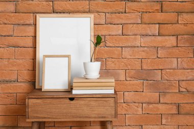 Boş çerçeveler, kitaplar ve ev bitkisi tuğla duvarın yanındaki masada.