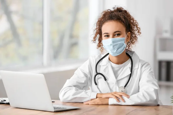 Female doctor wearing medical mask while sitting at table in clinic