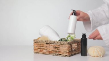 Kadın arka planda hediye sepetine spa malzemeleri koyuyor.