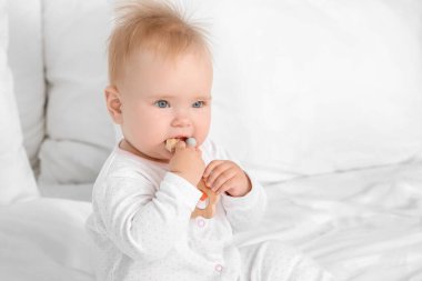 Yatağında diş çıkarma oyuncağıyla oturan tatlı bir bebek.