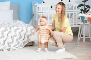 Anne küçük bebeğine evde yürümeyi öğretiyor.