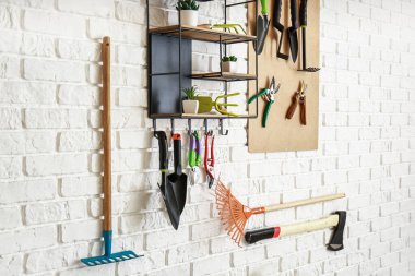 Ahırın duvarında farklı bahçe malzemeleri asılı.