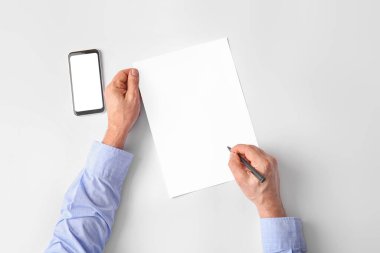 Açık arkaplanda cep telefonu ve boş kağıt kağıtlı erkek eller.