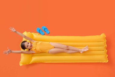 Cute little girl with headphones lying on inflatable mattress against color background clipart