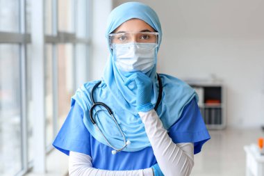 Klinikte koruyucu üniforma giyen kadın Müslüman doktorun portresi.