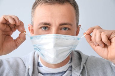 Gri arka planda tıbbi maske takan olgun bir adam.