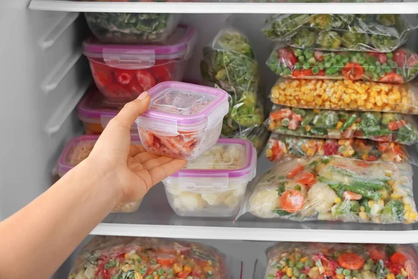 妇女将装有冷冻蔬菜的集装箱放进冰箱 — 图库照片