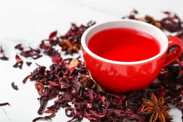 Cup and dry hibiscus tea on light background