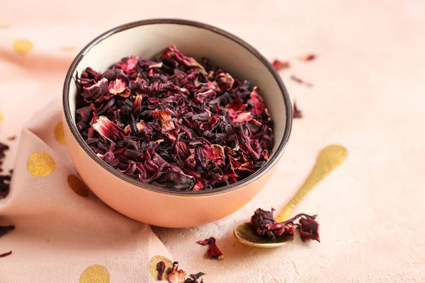 Bowl with dry hibiscus tea on light background