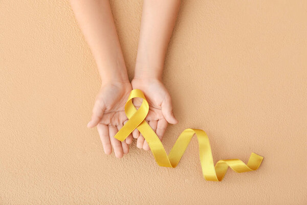 Child's hands with golden ribbon on color background. Cancer awareness concept