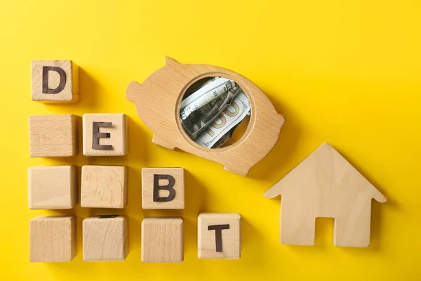 色の背景に単語Debtと家やキューブの図と貯金箱 — ストック写真