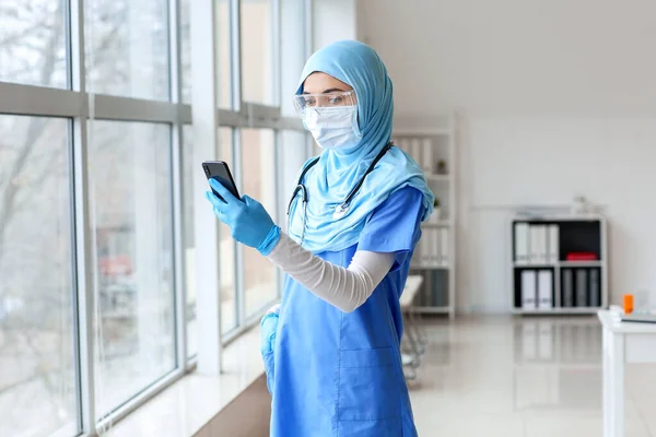 Female Muslim doctor with mobile phone in clinic