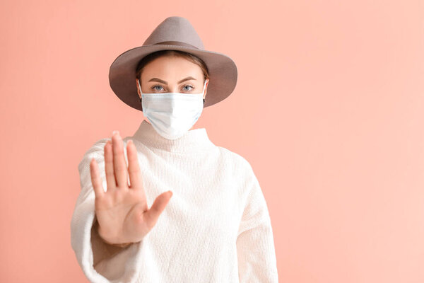 Young woman in medical mask showing STOP gesture on color background