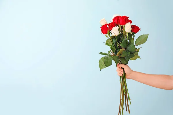 Hand with bouquet of beautiful roses on color background