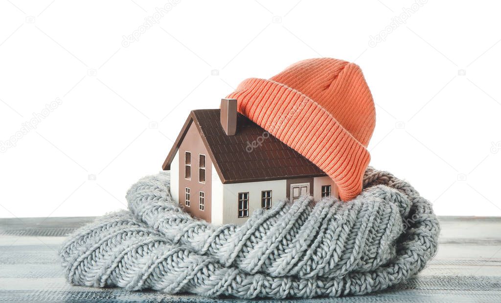 Figure of house and warm clothes on table against white background. Concept of heating season