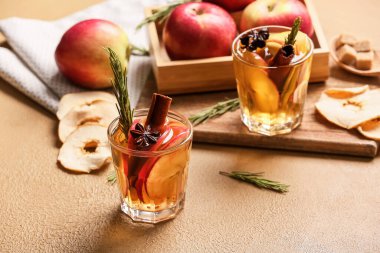 Renkli bardaklarda baharat ve elma dilimleri olan lezzetli bir içecek.