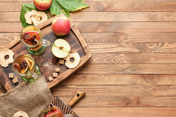 Tasty drink with spices and apple slices in cups on wooden background