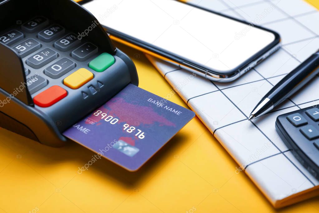 Payment terminal with credit card, notebook and mobile phone on color background