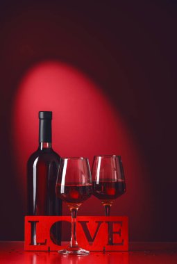 Bir şişe şarap, bardaklar ve koyu renk arka planda aşk kelimesi. Sevgililer Günü kutlaması