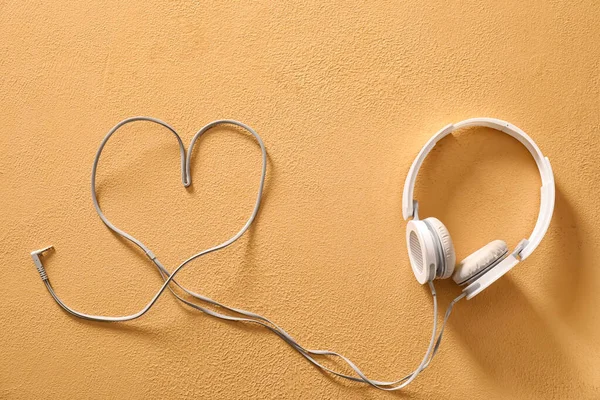 Modern headphones and heart made of wire on color background